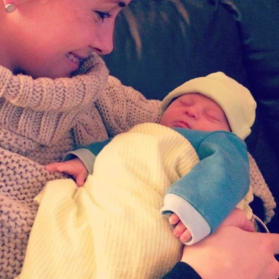 Woman smiles as she looks down at newborn with down syndrome asleep in her arms