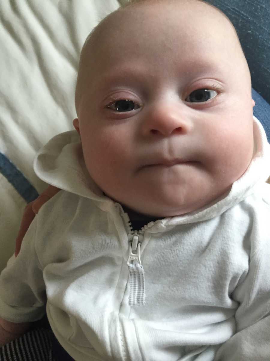 Close up of newborn with down syndrome wearing white zip up hoodie