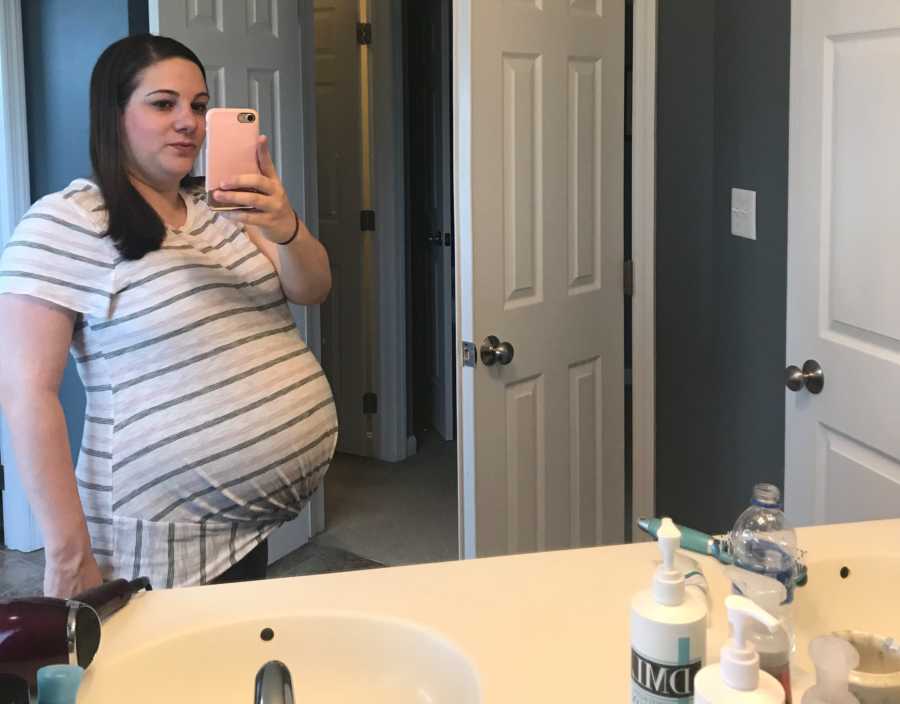 Mother pregnant with triplets stands in bathroom taking mirror selfie