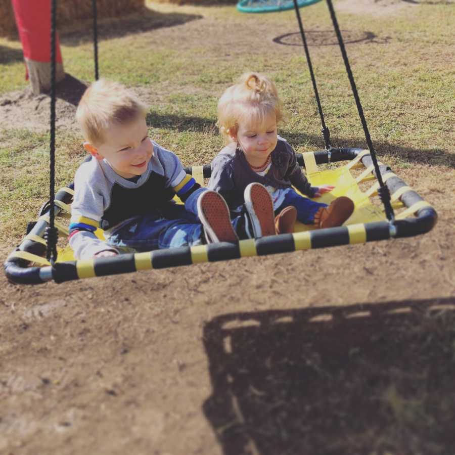 Two sibling in foster care sit on yellow and black swing