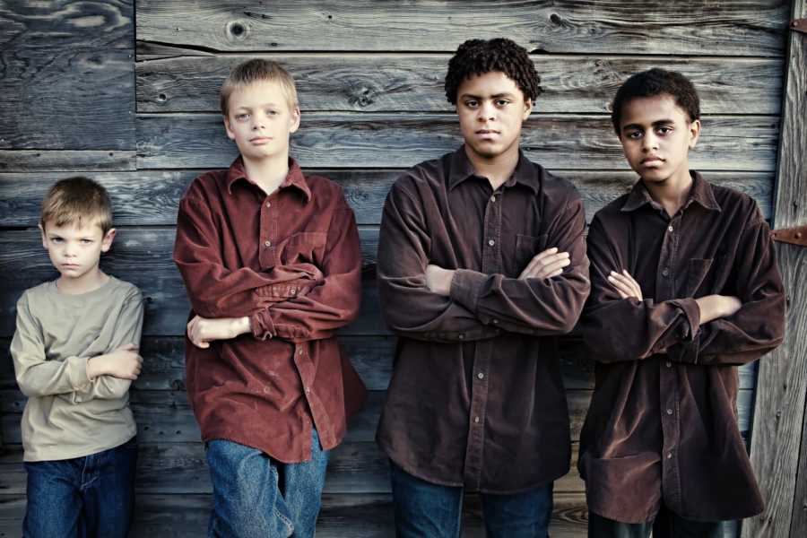 Four brothers lean against wood wall with their arms crossed