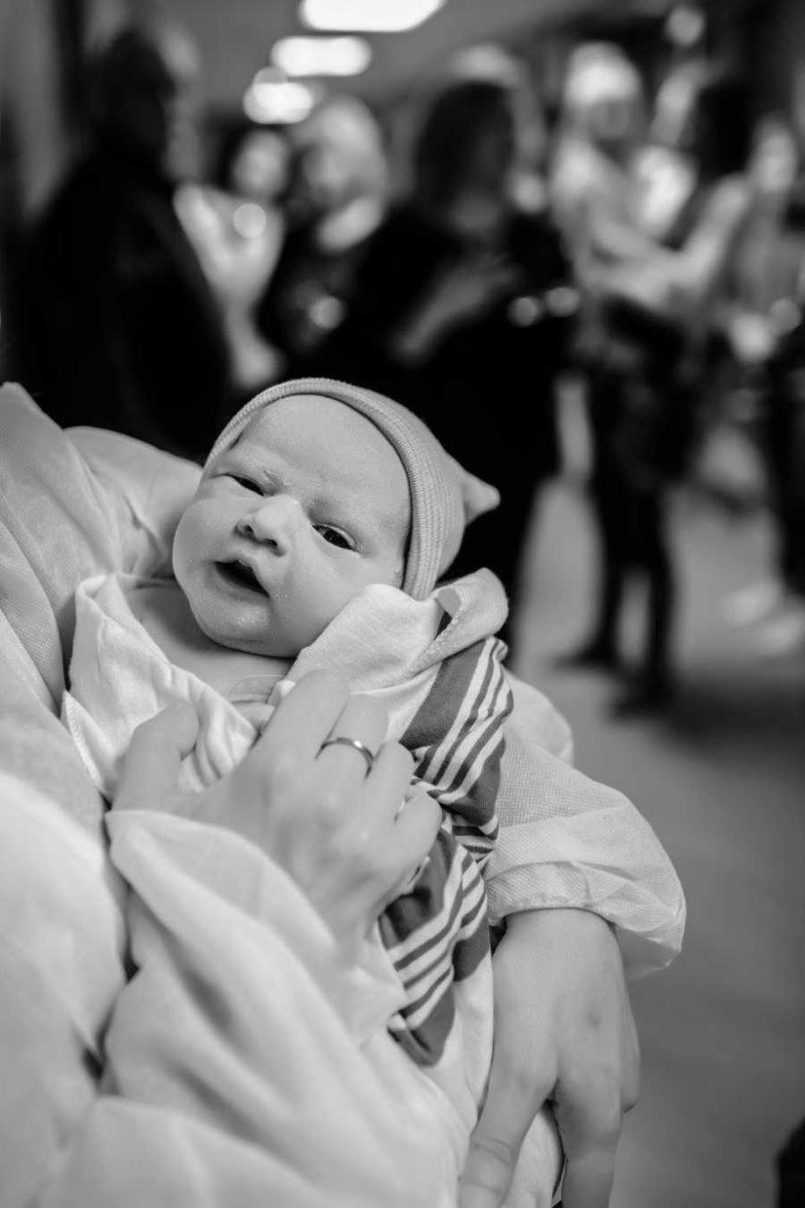 Close up of adopted newborn being held in woman's arms in hospital hallway