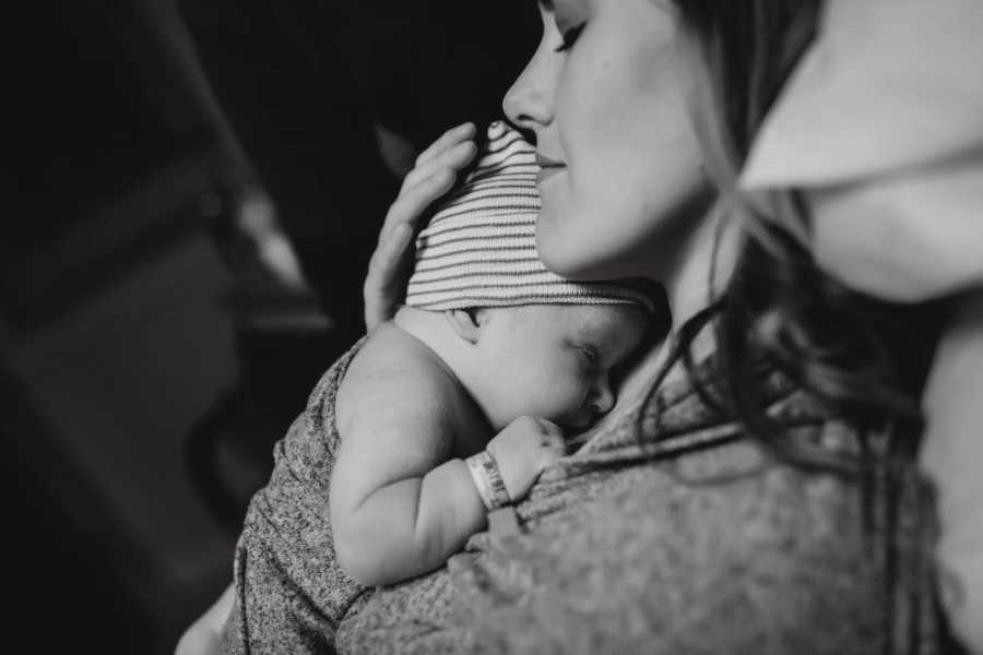 Mother sits in chair with eyes closed as she holds adopted newborn tight to her chest
