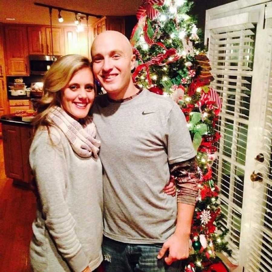 Man with leukemia who had bone marrow transplant stands smiling with wife in home in front of Christmas tree