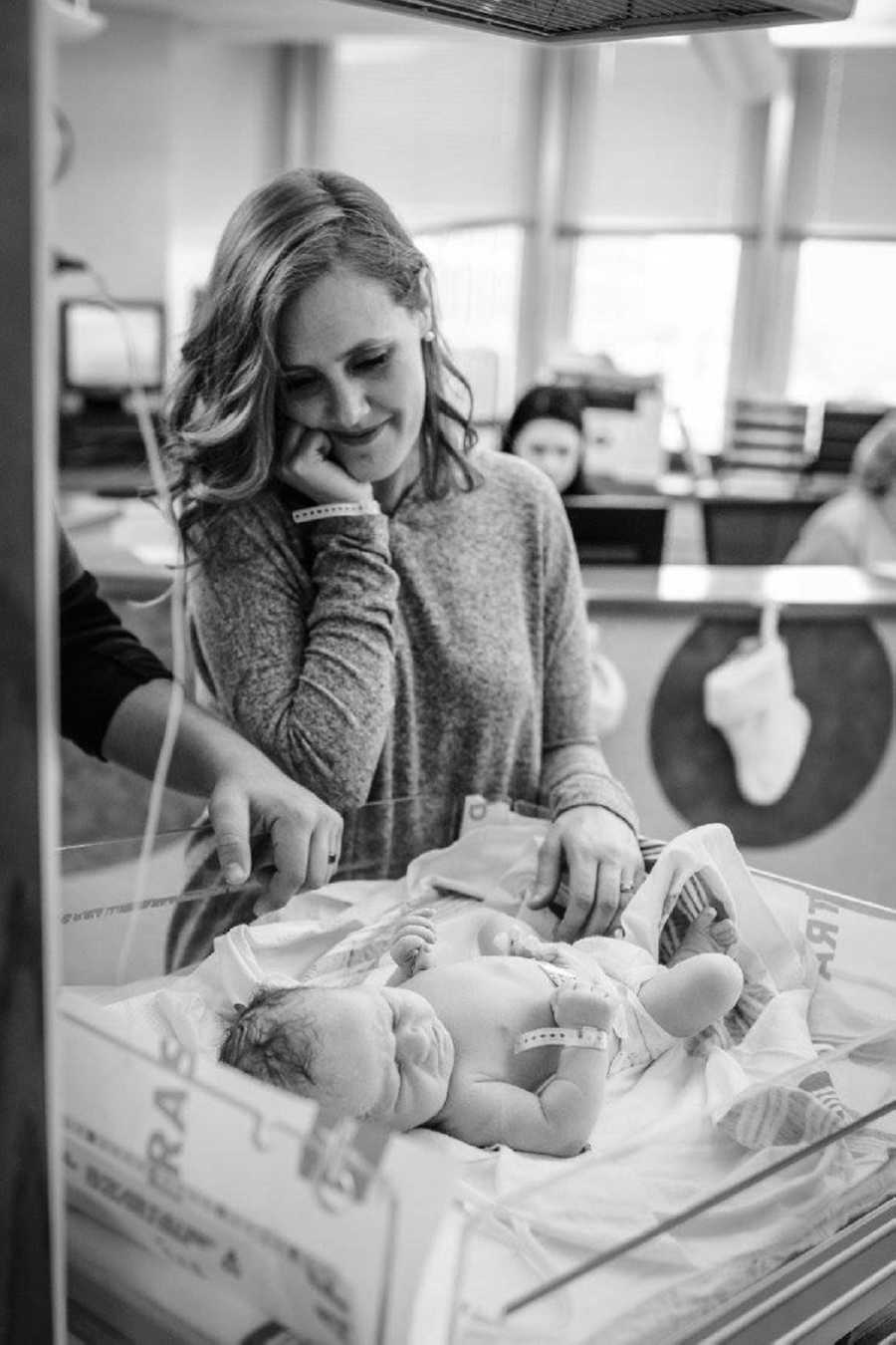 Mother stands smiling as she admires adopted newborn asleep on back