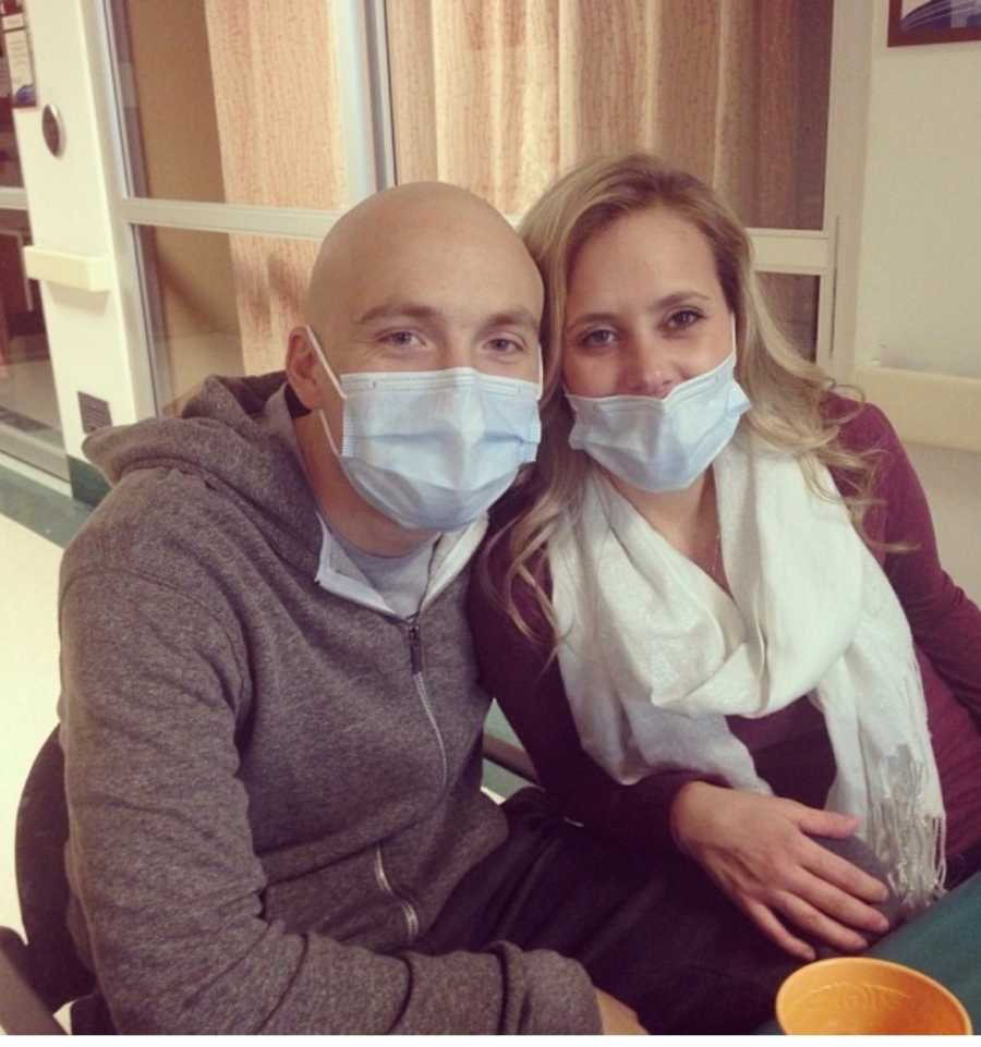 Man with leukemia sits in hospital with mask on beside wife who also wears mask