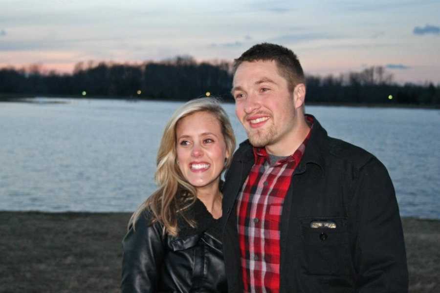 Couple smiles beside body of water after man proposes
