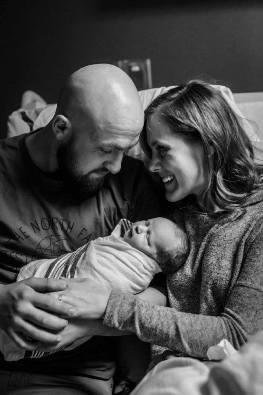 Wife smiles as husband as he holds adopted newborn boy