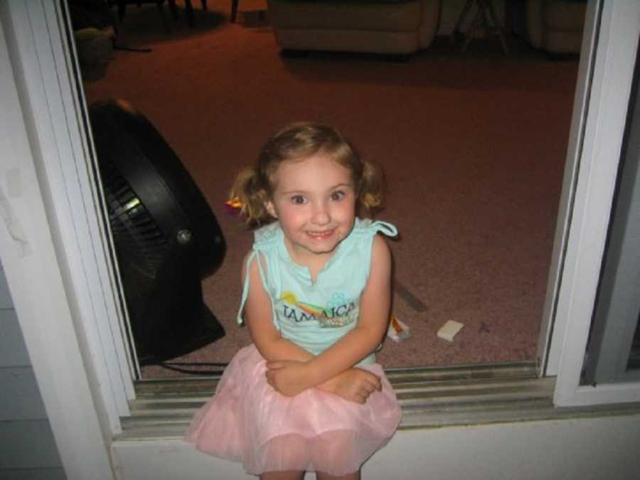 Little girl whose mother is an alcoholic sits on ledge of sliding door smiling