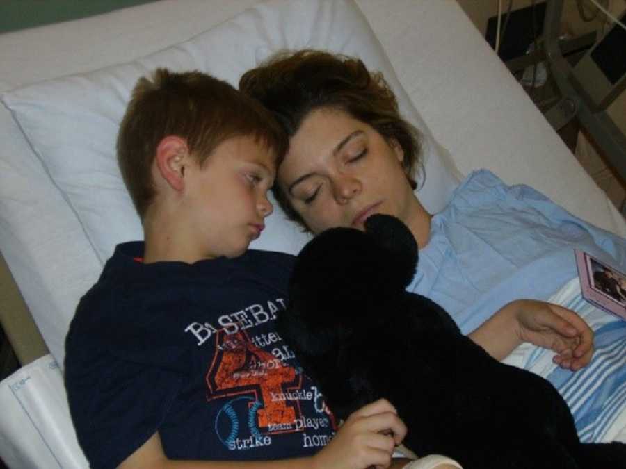 Woman lays asleep in hospital bed awaiting renal cell carcinoma surgery beside young son who looks over at her