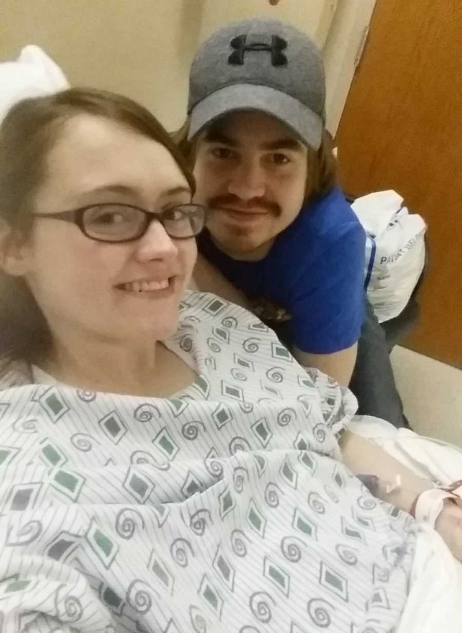 Woman with endometriosis smiles while laying in hospital bed with husband by her side in selfie