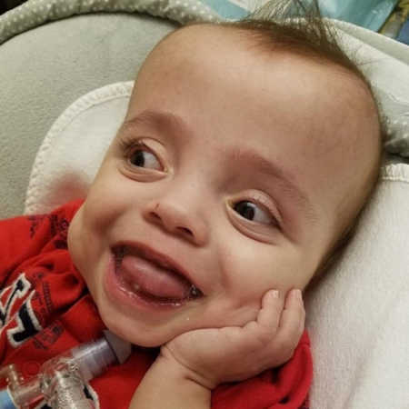 Baby with trach smiles while laying in PICU