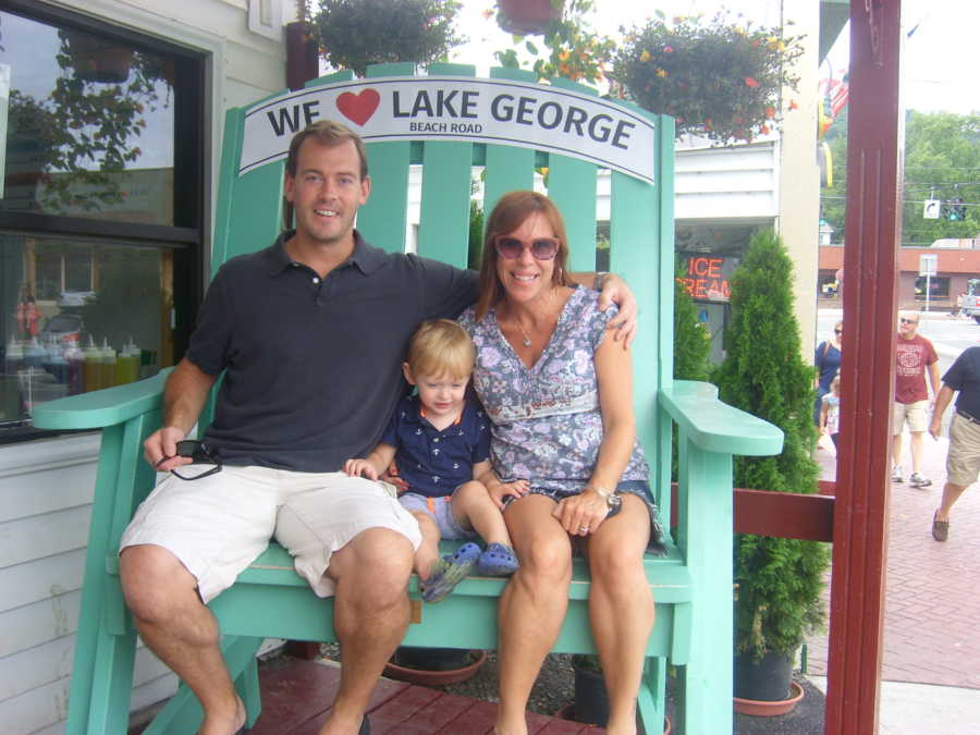 Husband sits with son and pregnant wife in large Adirondack chair that says "We heart Lake George"