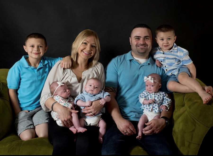 Husband with Chiari Malformation and wife sit on green couch with baby triplets on their laps and two older sons at their side