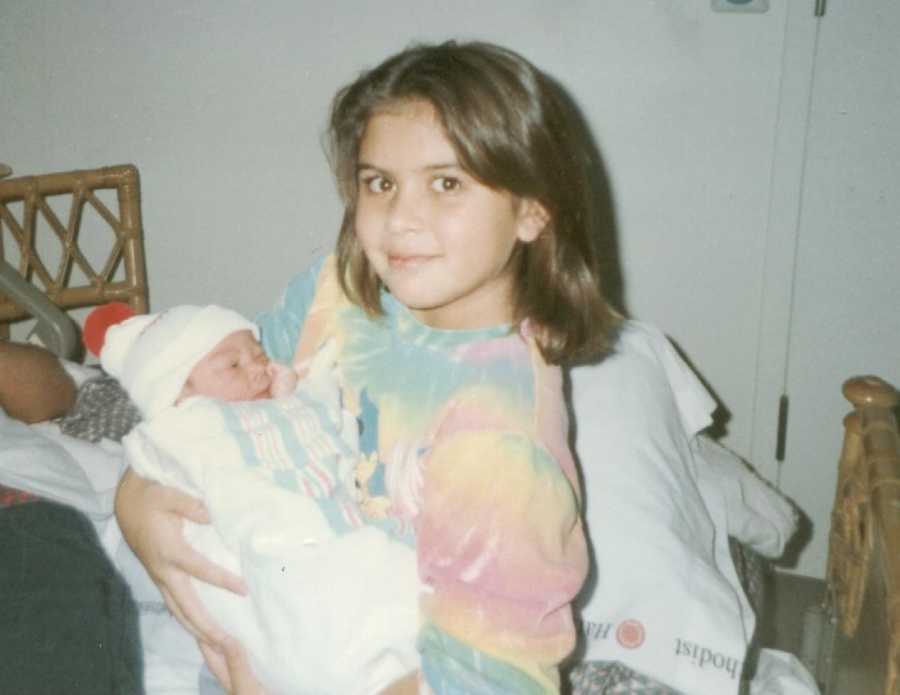 Older sister who has since passed from committing suicide sits in chair in home holding swaddled baby sister