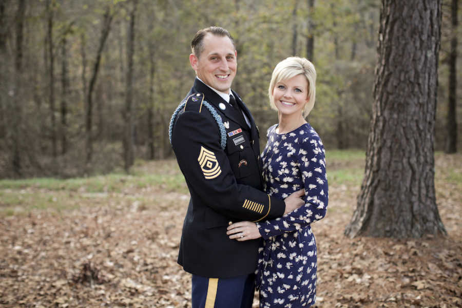 Army husband and wife stand arm in arm outside smiling 