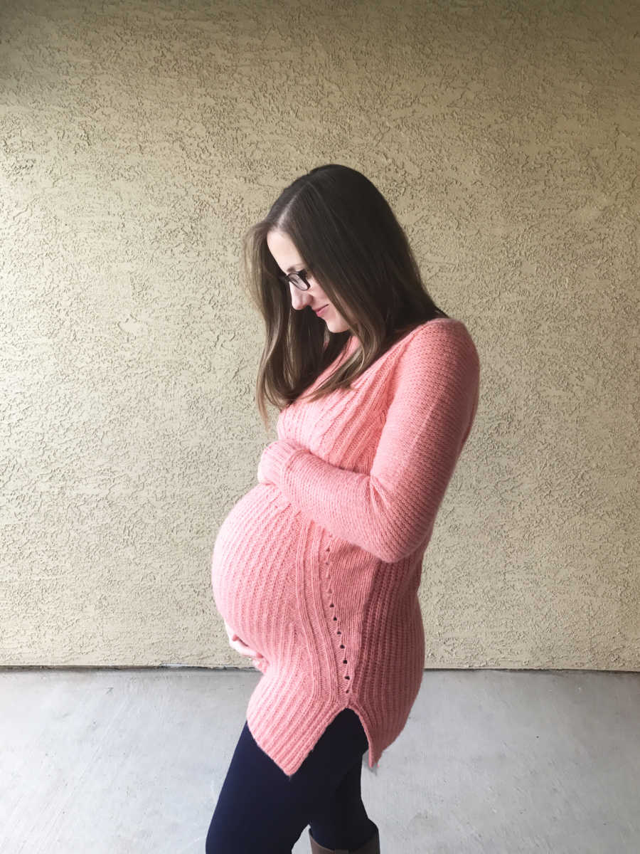 Pregnant woman stands outside holding her stomach