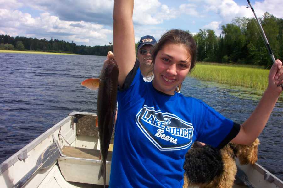 Teen smiles as she stands in boat holding up fish she caught