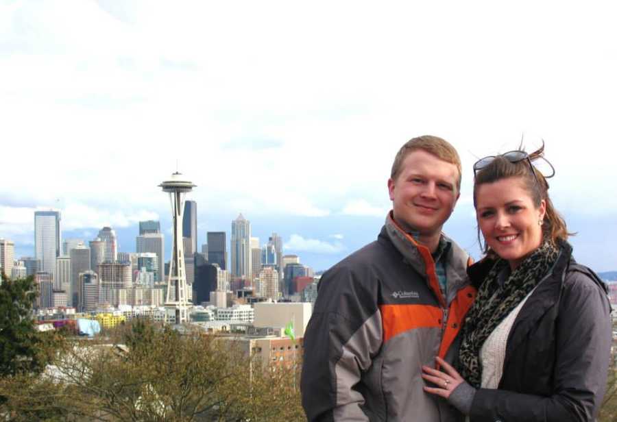 Husband and wife stand arm in arm with Seattle skyline in background