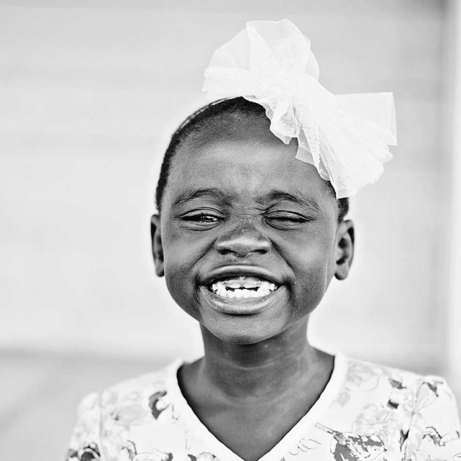 Young orphan girl smiles as she wears big white bow on her head