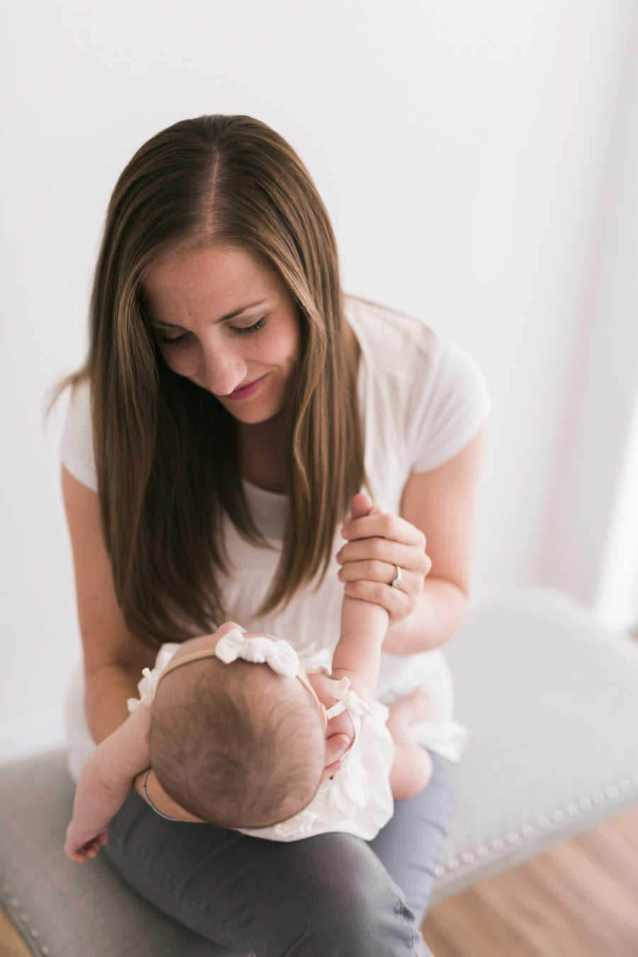 Mother sits on bench looking down at baby daughter with down syndrome in her lap