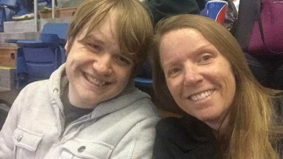 Woman smiles in selfie sitting beside teen son in stadium seats