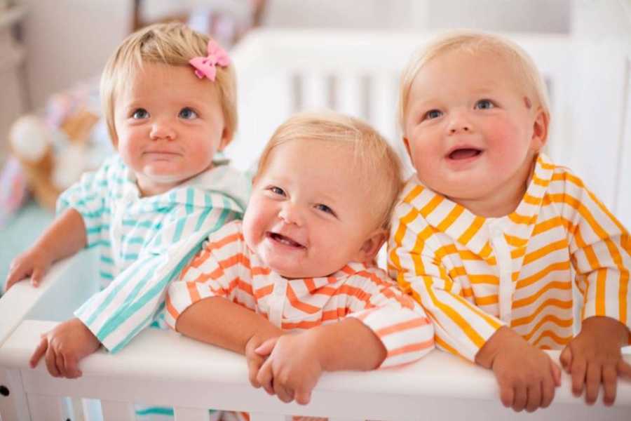 Triplets stand smiling in crib