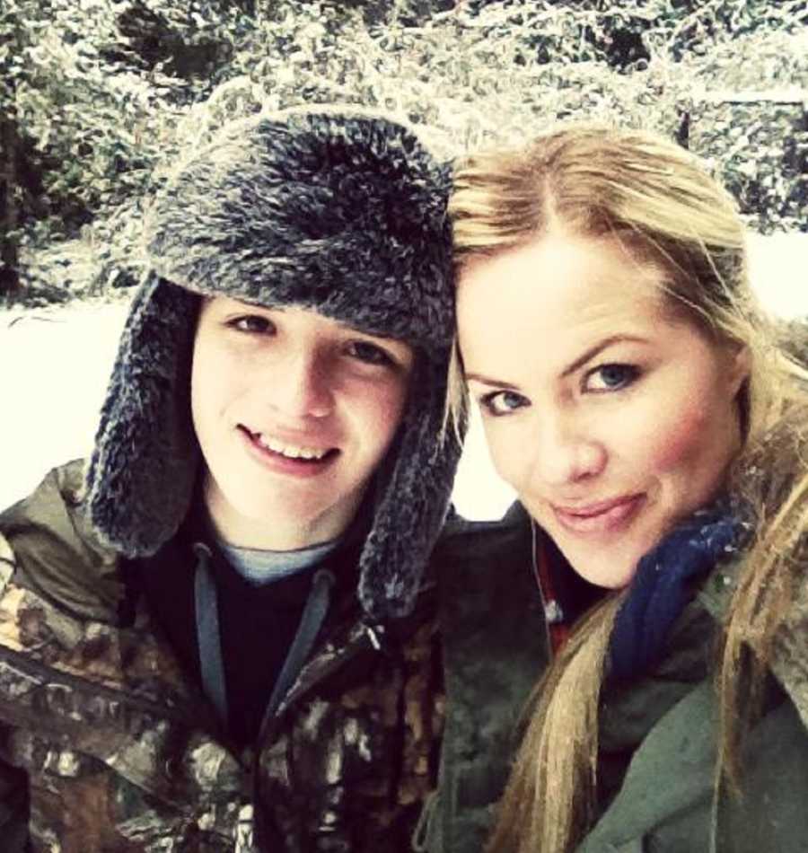 Mother stands outside in snowy weather smiling beside teen son in selfie