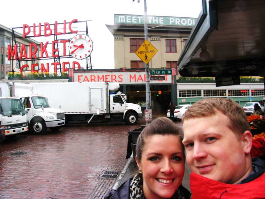Husband and wife smile in selfie with Public Market Center sign in background