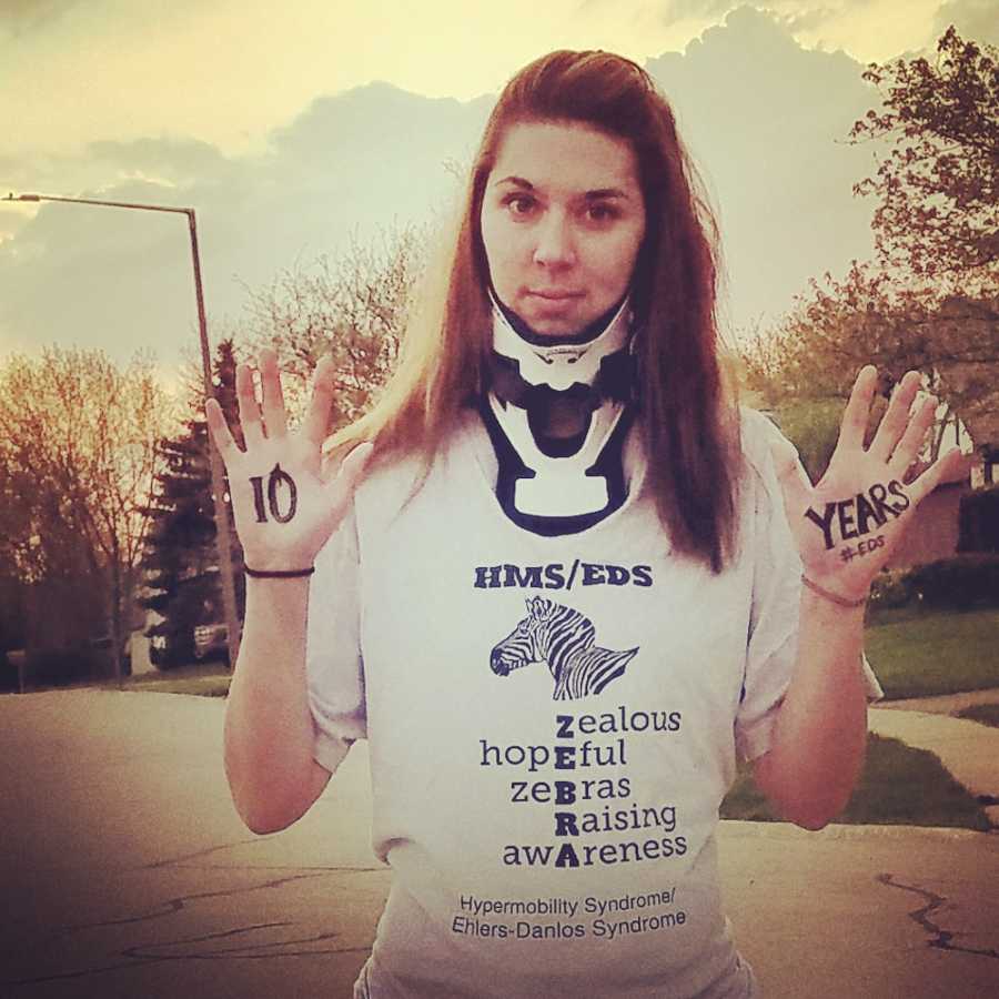 Young woman with Ehlers-Danlos Syndrome stands outside wearing neck brace and hands in air