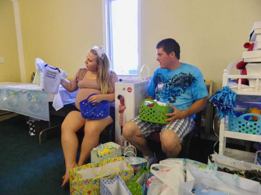 Pregnant husband and wife sit in chairs opening presents at baby shower