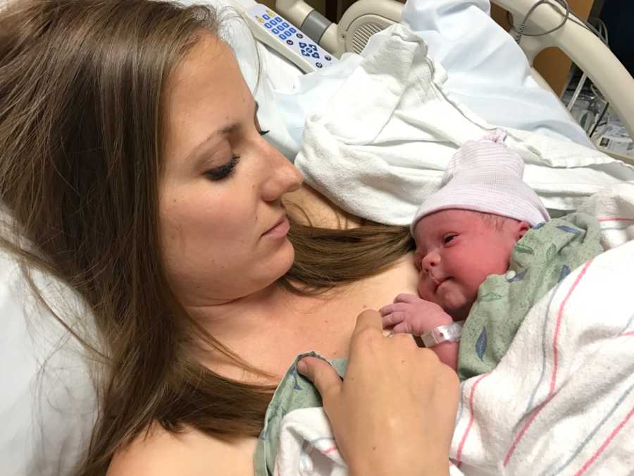 Woman lays in hospital bed looking down at newborn who lays on her bare chest