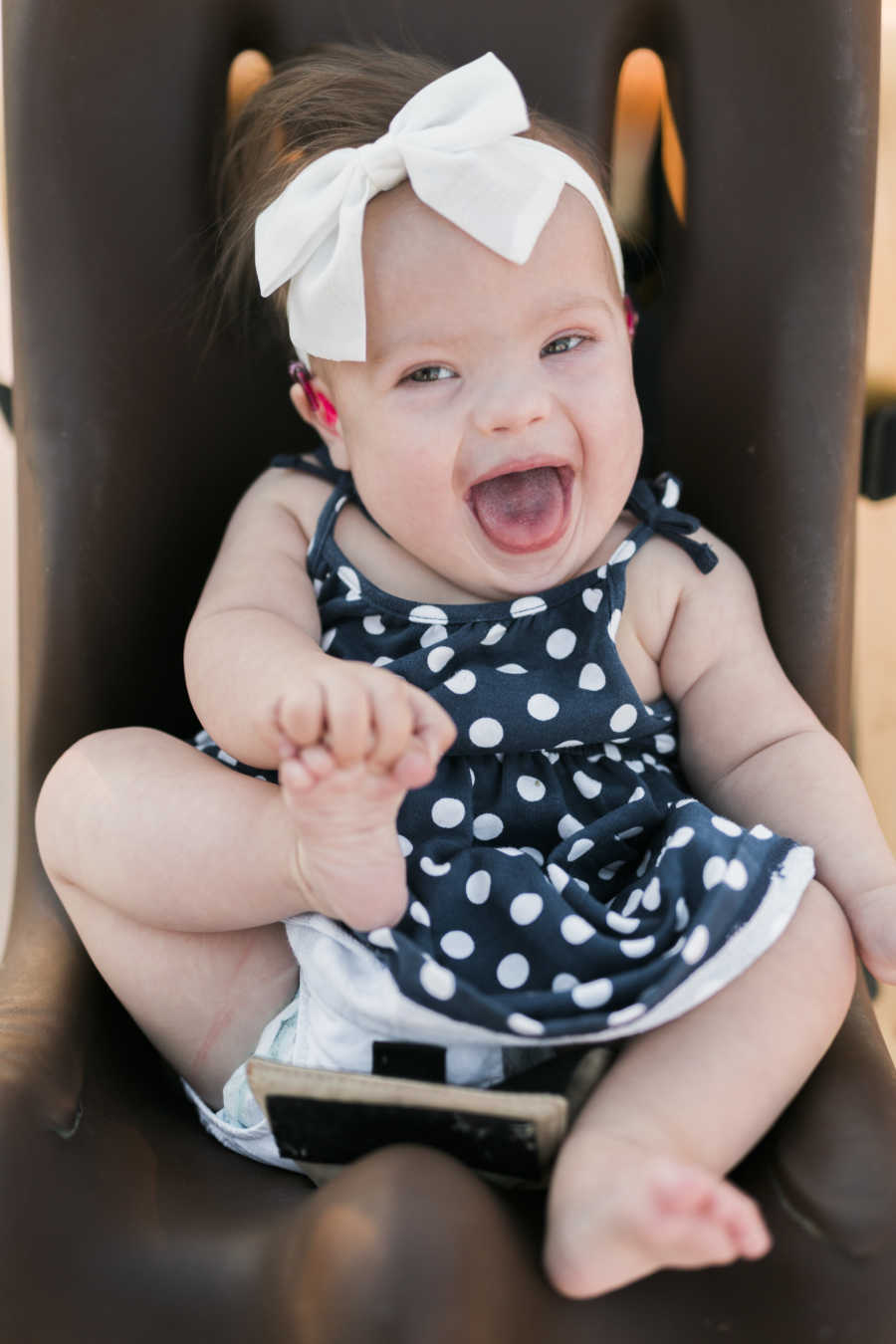 Baby with down syndrome and heart defect sits smiling holding onto her foot