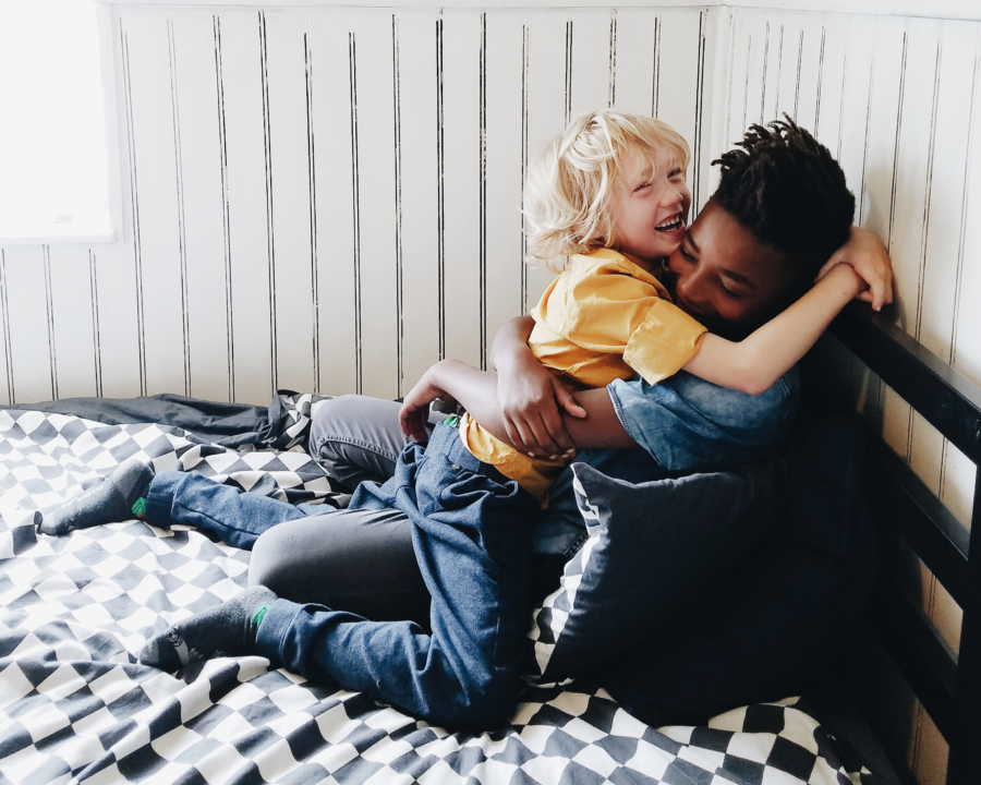 African American boy sits in bed hugging white little brother who sits on his lap