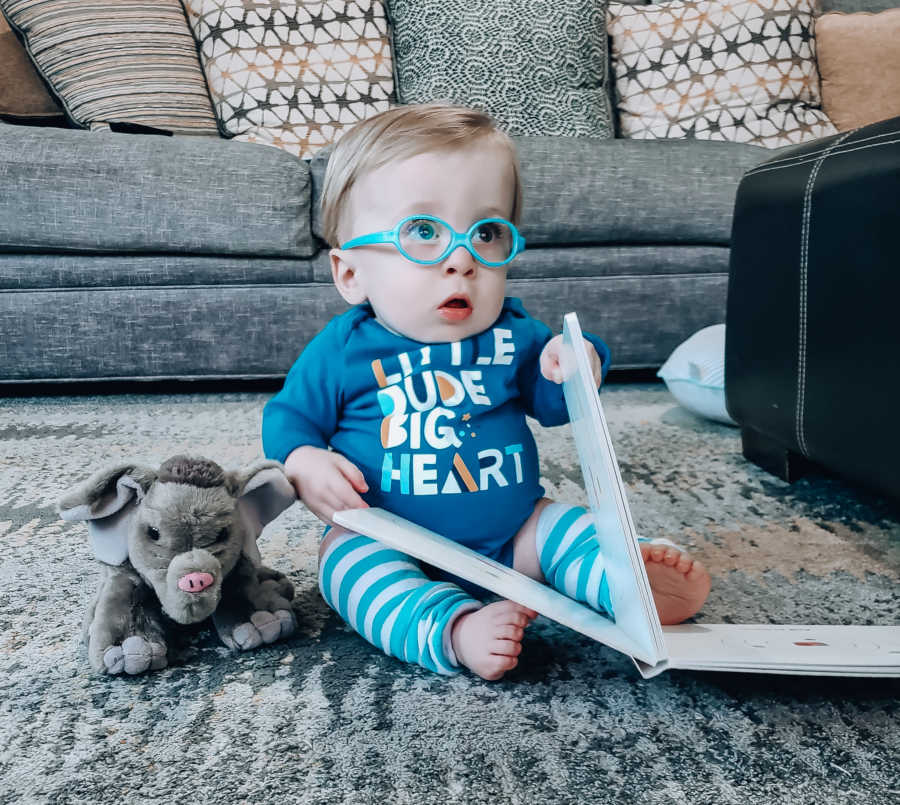Baby boy with dwarfism sits on floor of home holding onto book