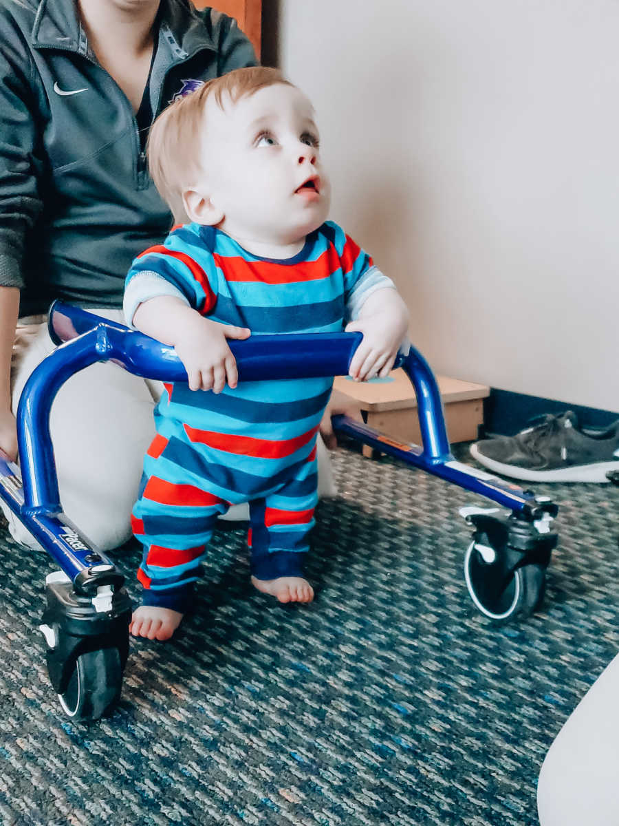Baby boy with dwarfism stands holding onto walker