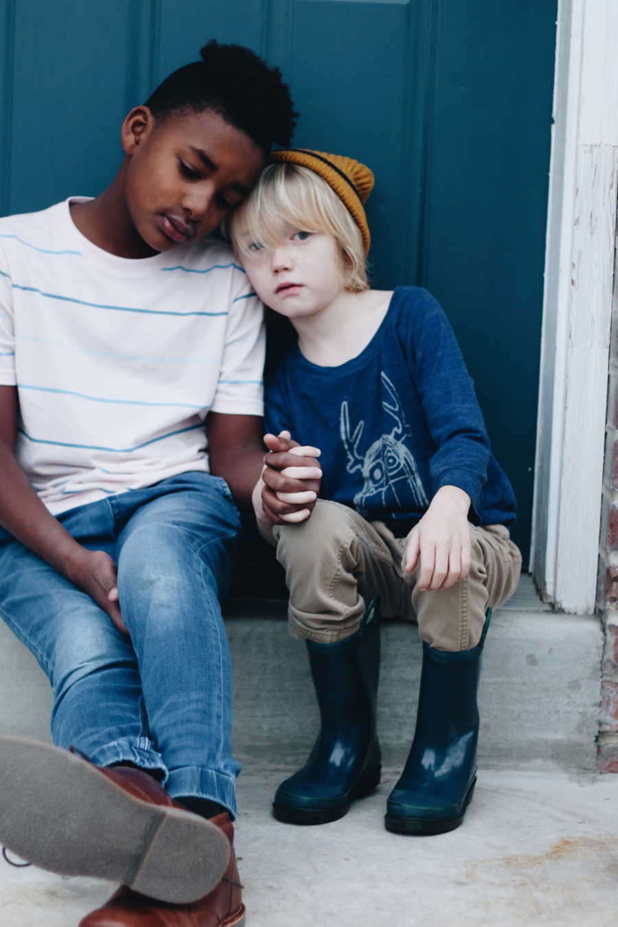 African American boy sits beside white little brother on step holding his hand