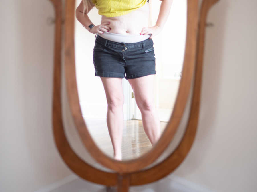 Lower half of woman's body in mirror with stomach exposed