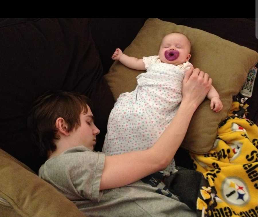 Young man lays asleep on couch beside his baby niece