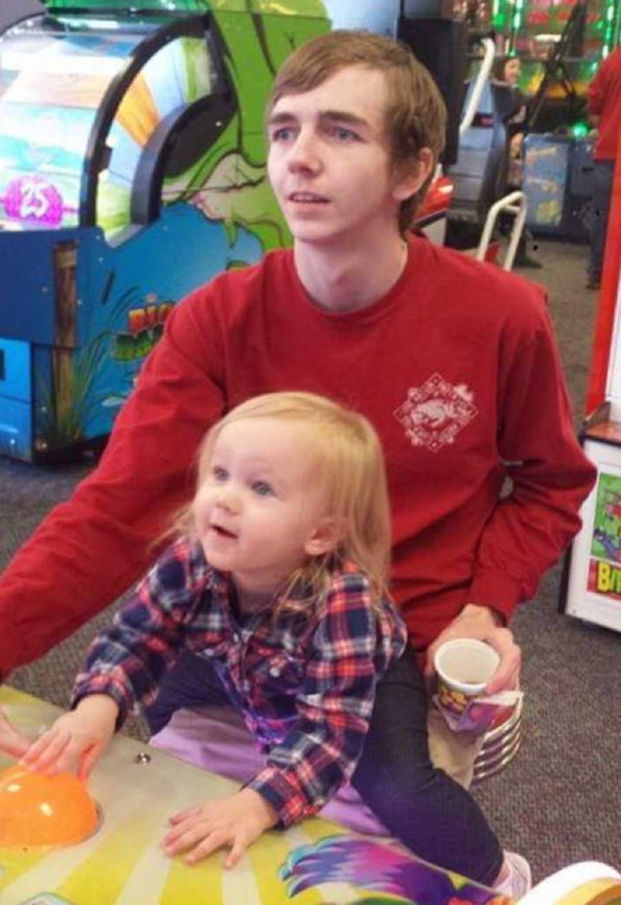 Young man who will become addicted to drugs sits at arcade game with niece in his lap