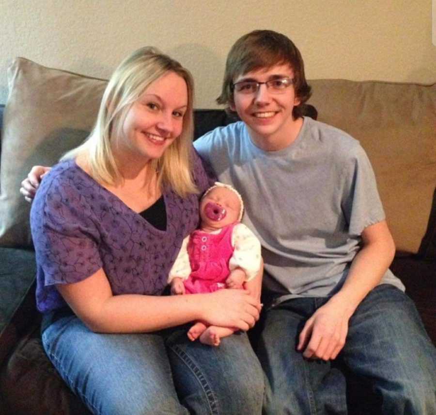 Woman sits on couch with baby daughter in her lap and her brother beside her