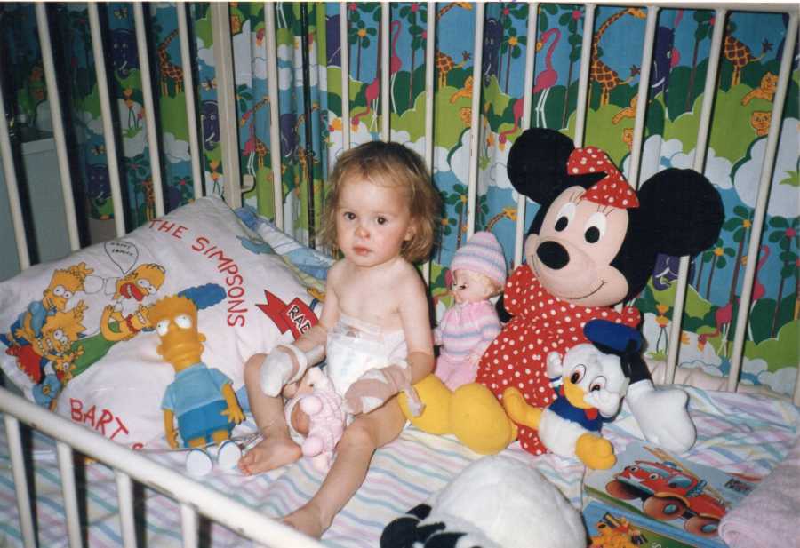 Baby girl with Exomphalos sits in crib with stuffed animals