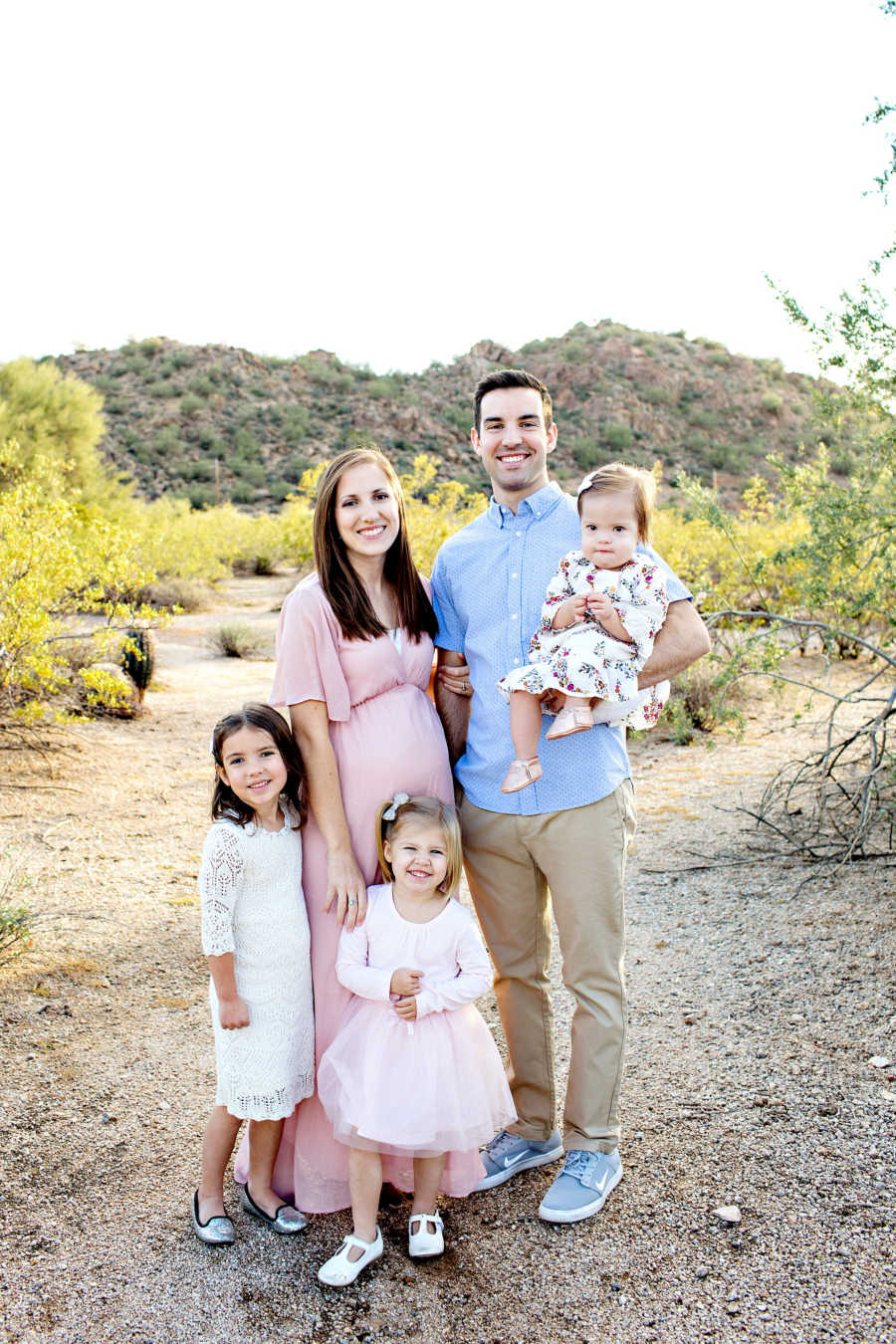 Wife stands outside beside husband who holds daughter with down syndrome and their two other daughters in front of them