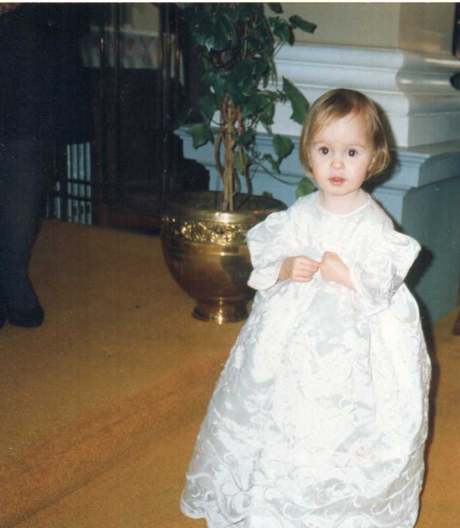 Little girl with Exomphalos stands in white dress for christening
