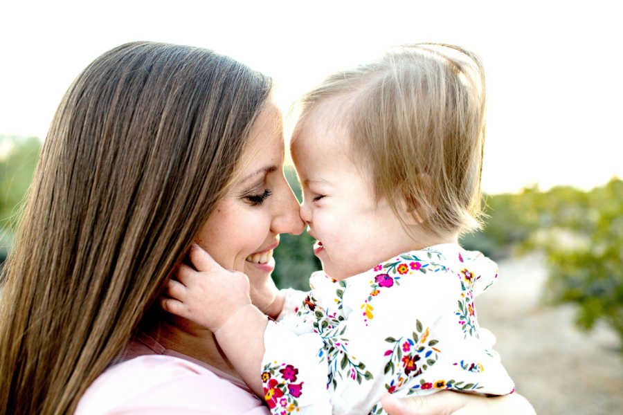 Baby with down syndrome and heart defect holds mom's face as their noses touch