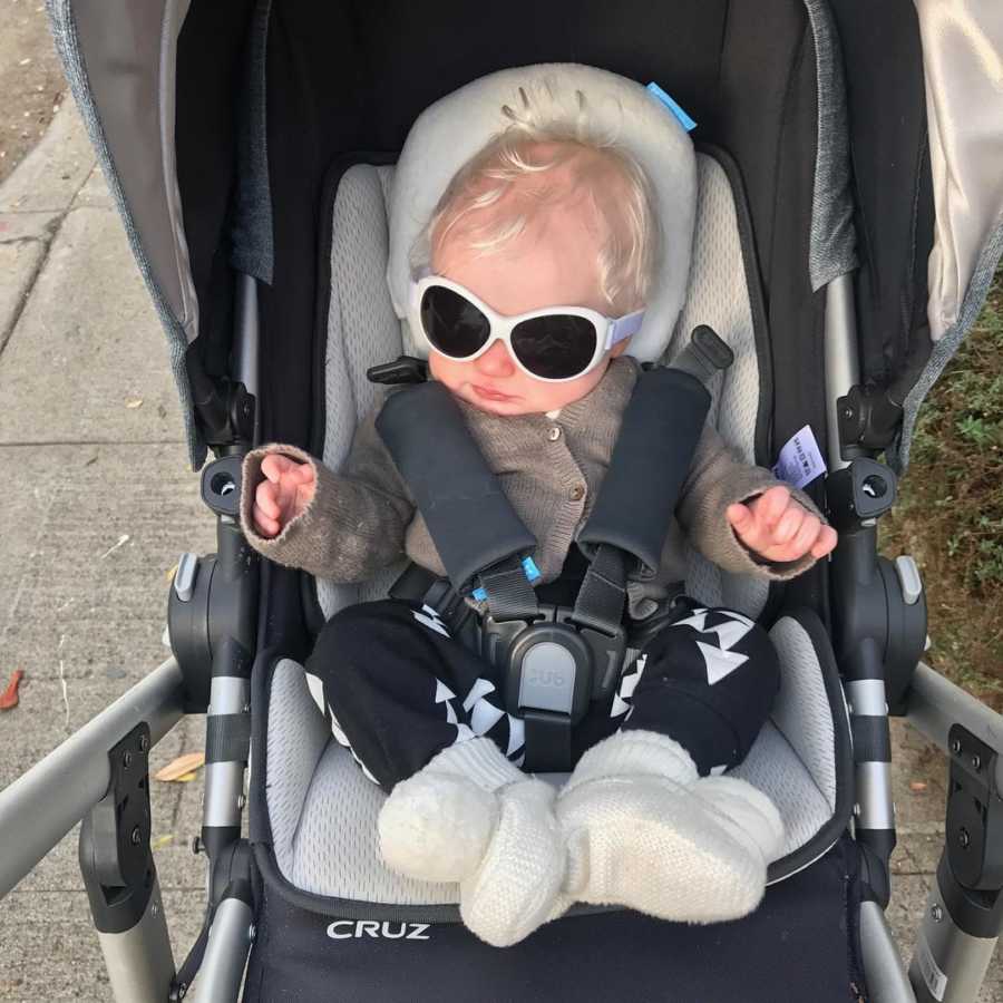 Albino baby sits in stroller with big white sunglasses on