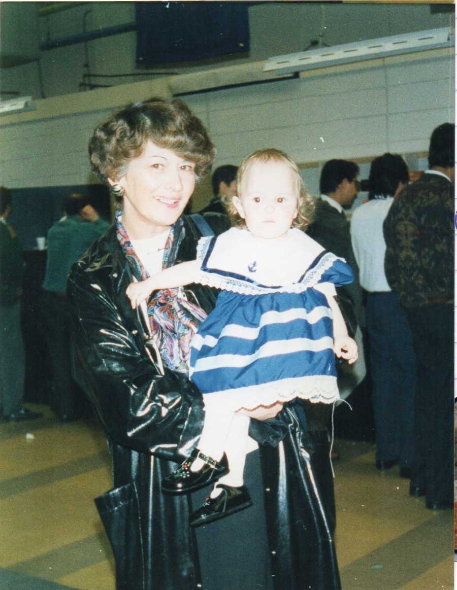 Little girl with Exomphalos wears blue and white stripe dress while being held by grandmother