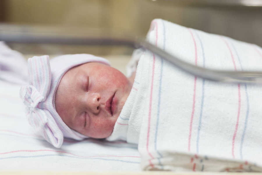 Newborn baby girl lays asleep swaddled in blanket in hospital