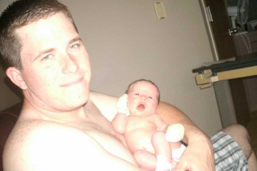 Shirtless father sits in hospital holding newborn