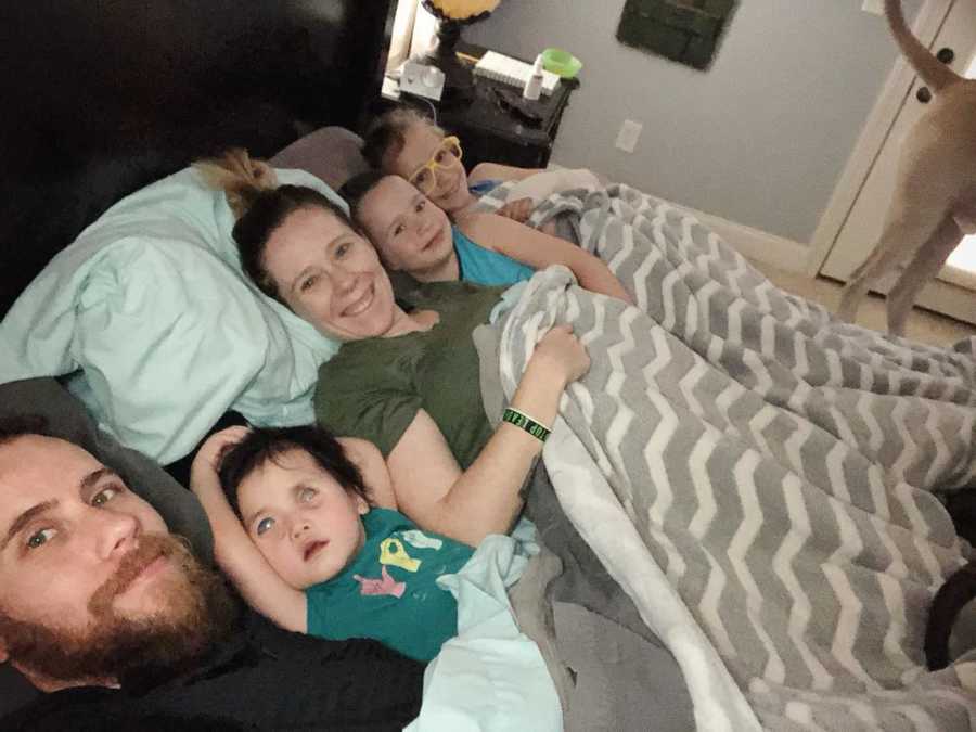 Husband and wife lay in bed with two biological kids and their adopted daughter who is blind and deaf